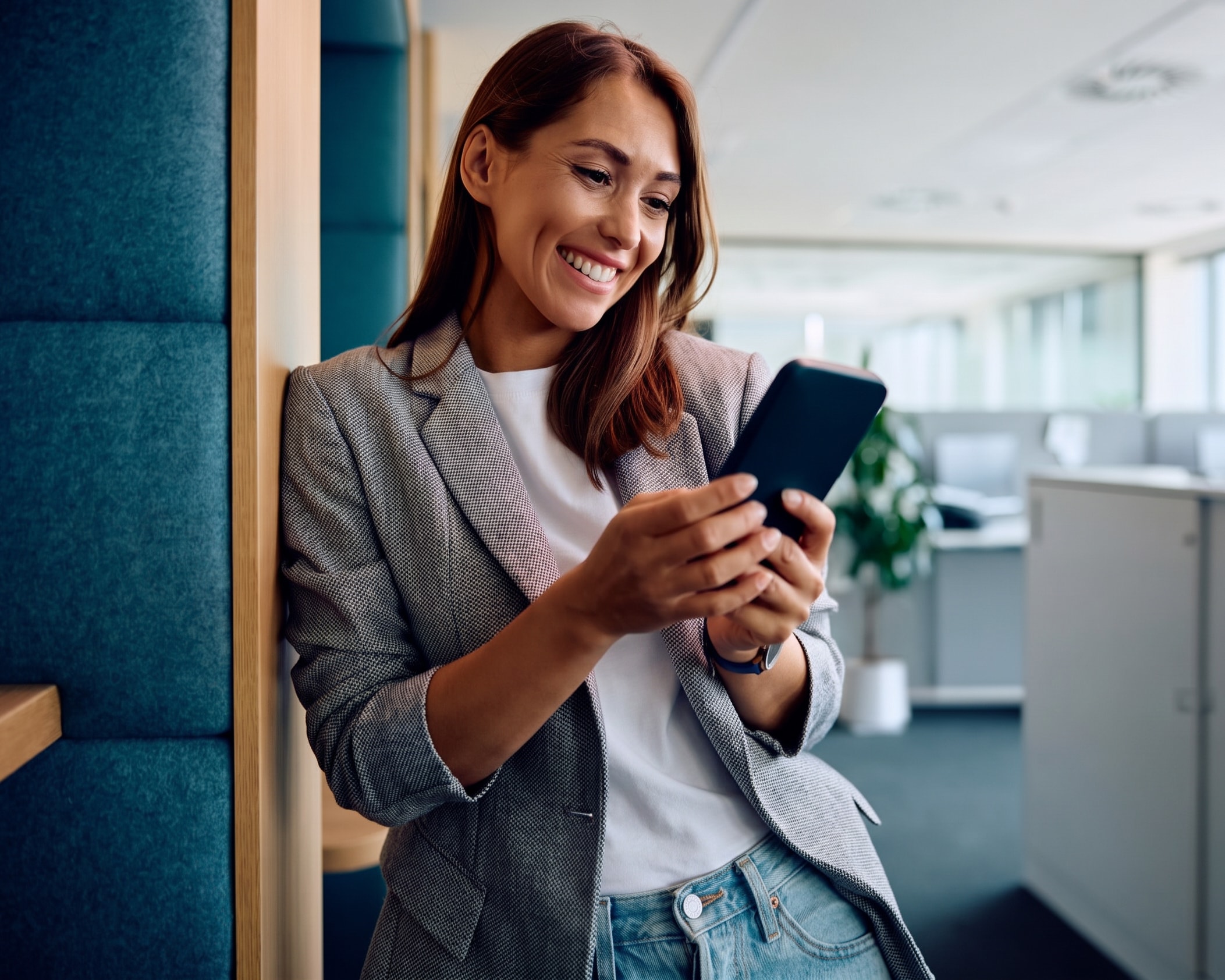 Mulher sorrindo enquanto usa o celular no escritório